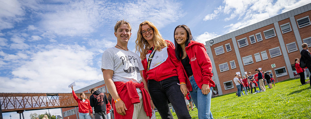 Tre glade studenter utenfor campusbygninger